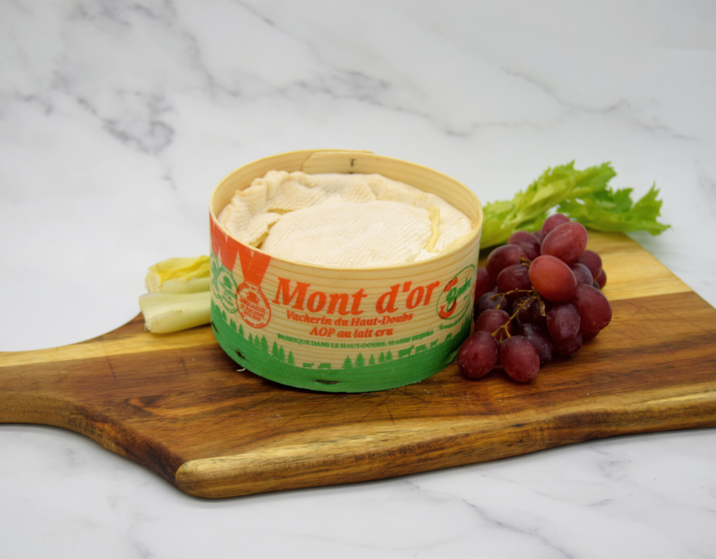 Vacherin Mont D'or in its box no lid on a wooden board with grapes and celery 